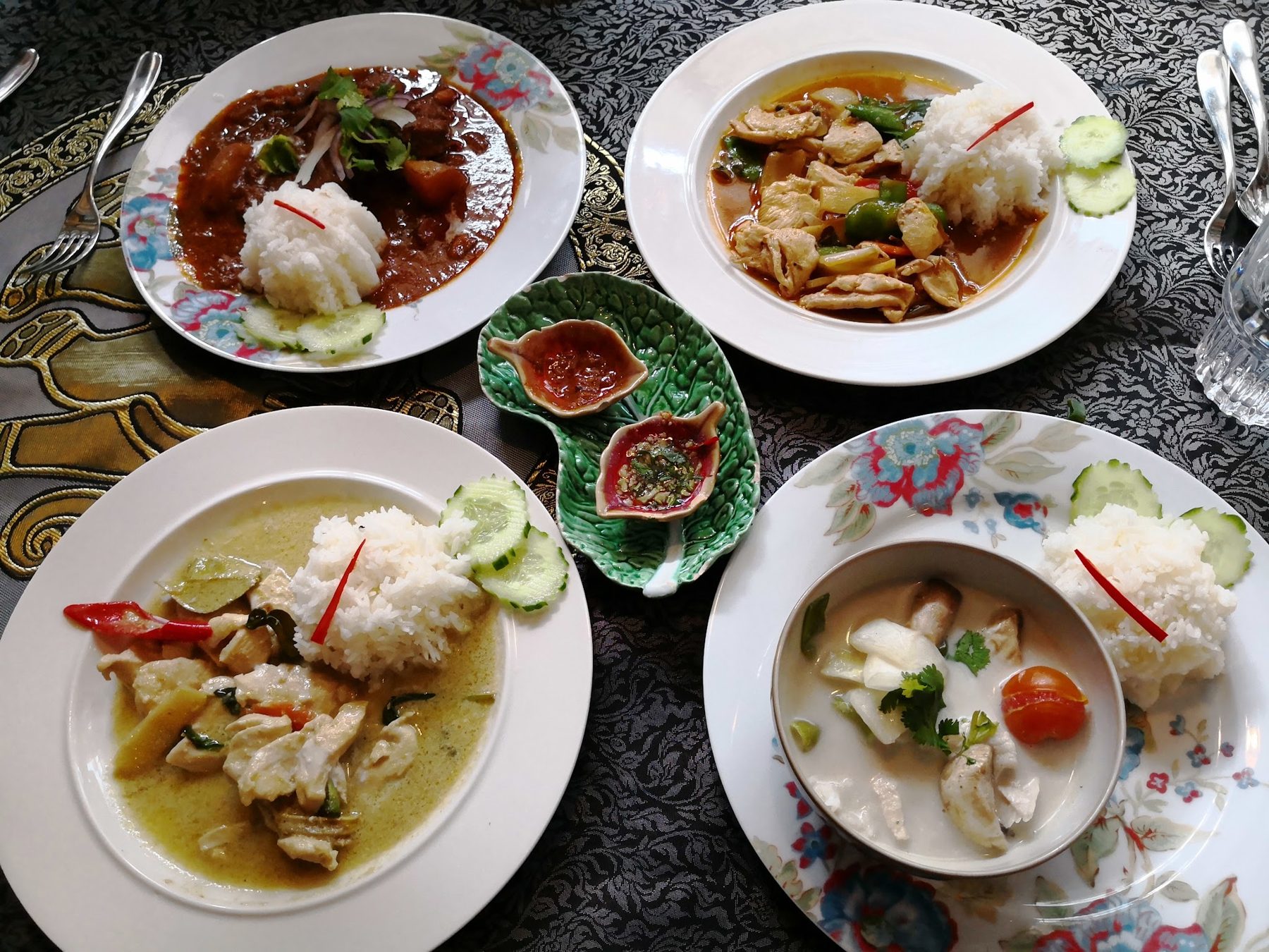 Four Thai dishes on white plates on a dark table