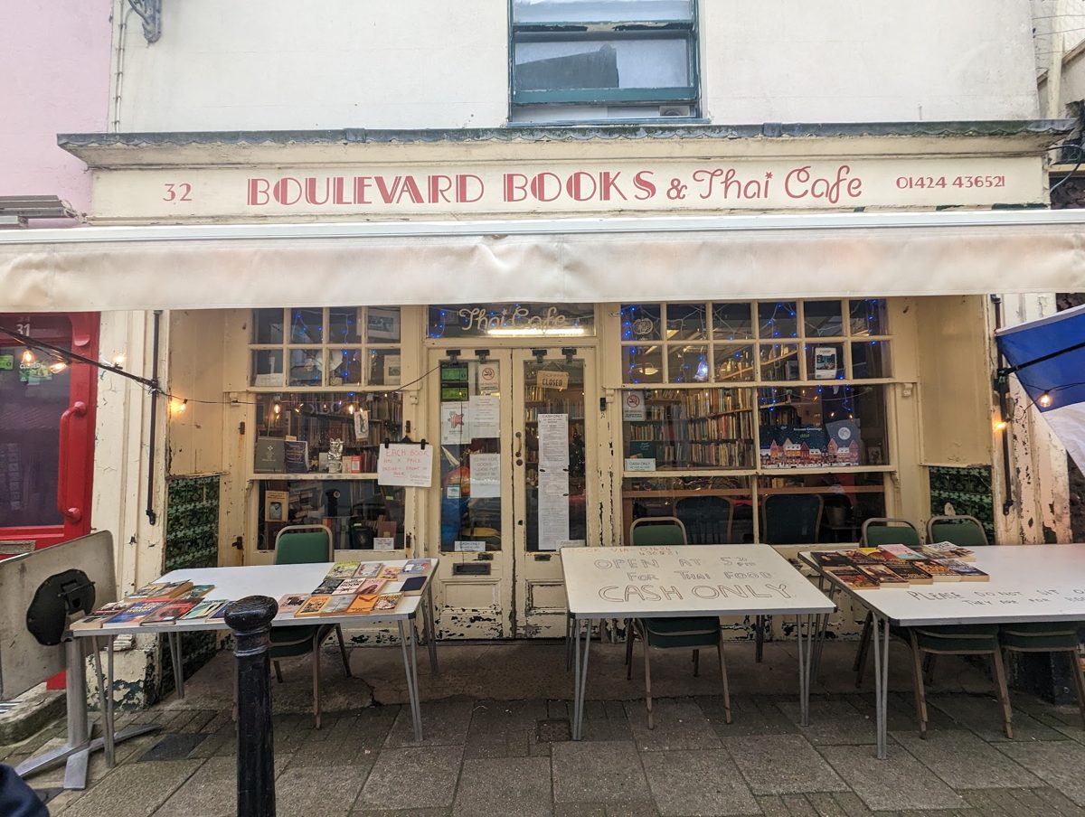The cream shopfront with the red Boulevard Books & Thai Cafe fascia and tables outside
